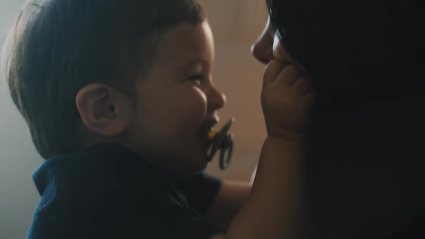 A boy squeezes his moms cheeks while sitting in her lap
