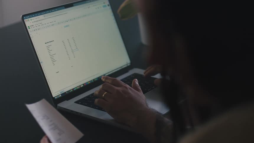 A woman watches as a man uses a spreadsheet on his laptop