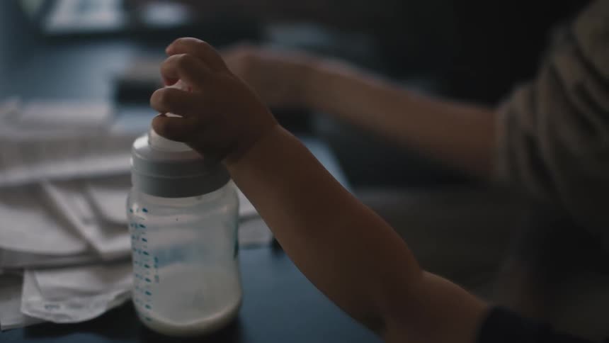 An up close of a babies hand on an almost empty milk bottle next to someone else