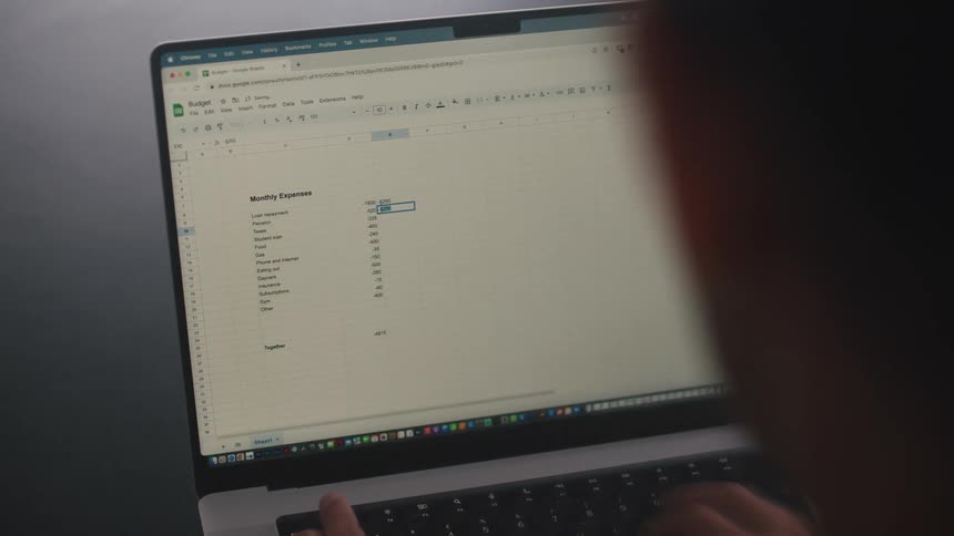 A close up of a person using their laptop typing on the keyboard into a spreadsheet