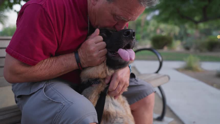 Man giving his dog a kiss while sitting on a bench in a square