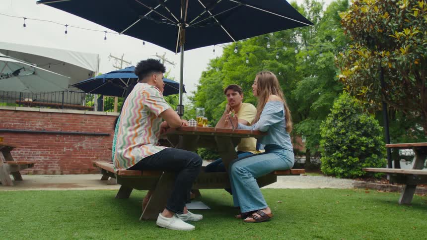 Group of friends sitting at a table with umbrella and trees around