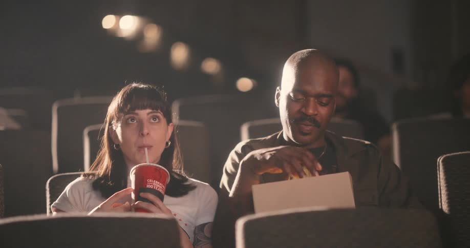 A man and a woman share popcorn in a movie theater