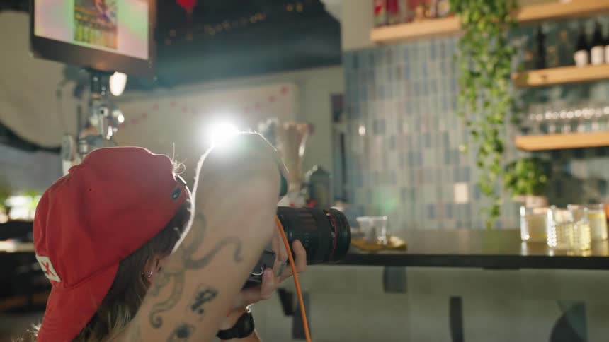 A woman photographs an employee at a bar pouring water into a cup