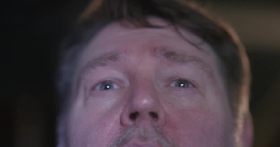 A mans face lit by flashing lights