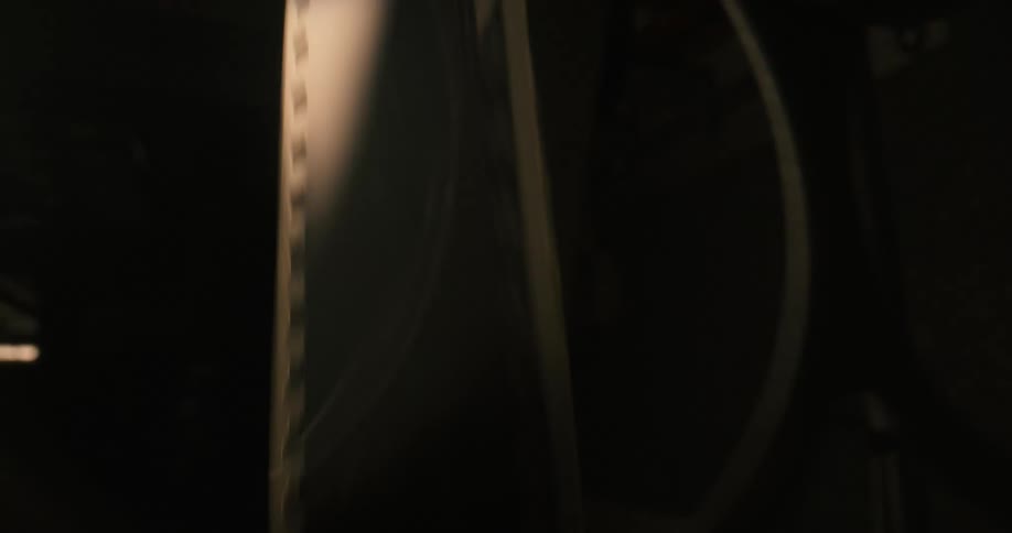 A closeup view of a strip of film with perforations along the edge rolling in front of a strobing light in a dimly lit room