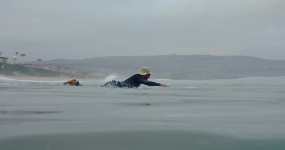 A man paddles out into the ocean on a surfboard near a resort on the coast