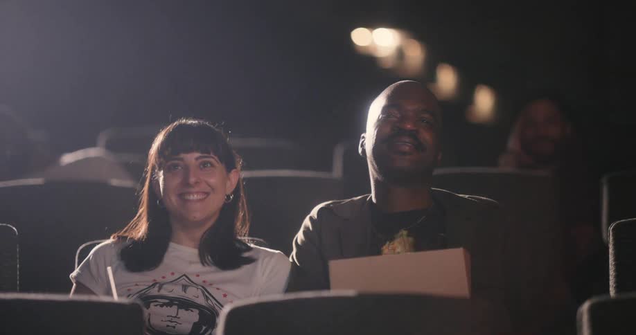 Man and woman on a date smile at each other while enjoying a movie at the cinema