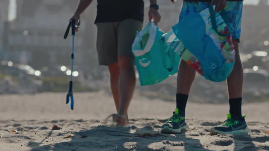 Two men talk while collecting trash on a beach
