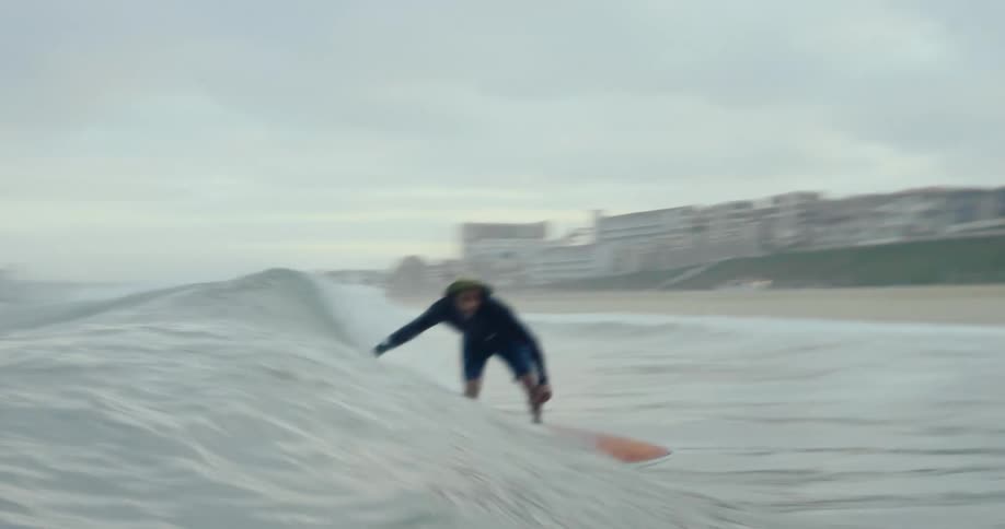 Surfer stands on his surfboard and rides it towards the beach until he falls while mist covers the town in the background