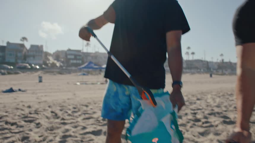 Two men walking on the beach sand with bags and collecting trash
