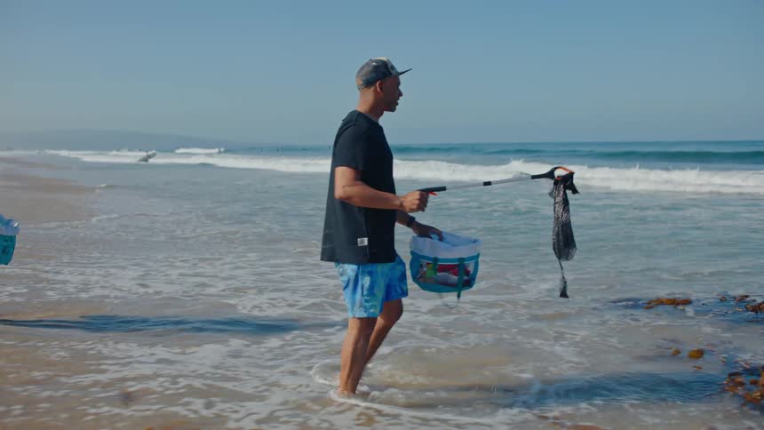 Two men trying to collect garbage from a beach before the waves take it away