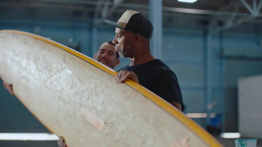 A man hands a surfboard to another man
