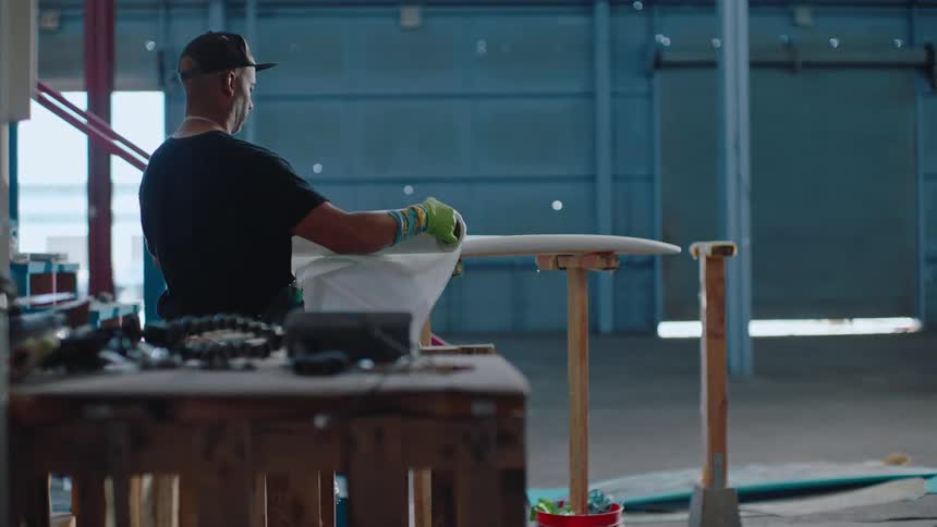 Worker in a workshop applies wrapping to a surfboard