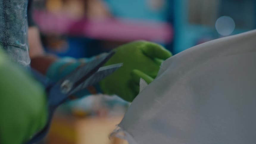 Close up of a pair of hands with green gloves using scissors and cutting white fabric