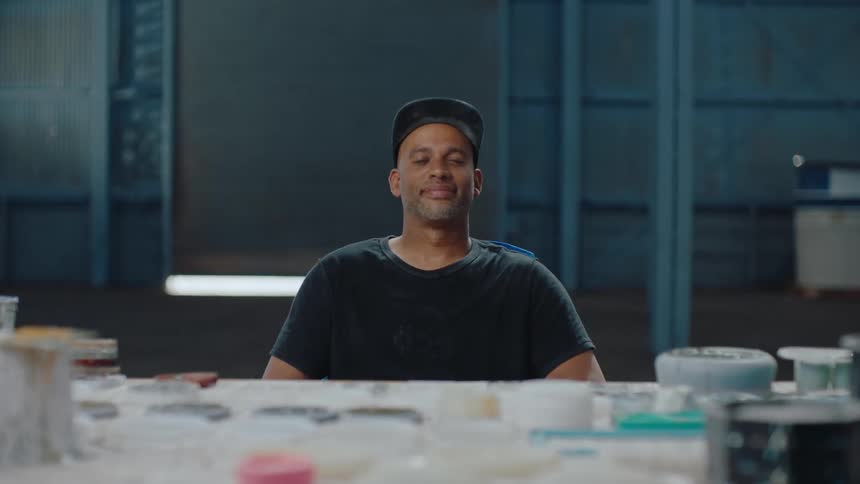 Portrait of a man with a facial expression of unhappiness sitting at a table with paint divided into jars
