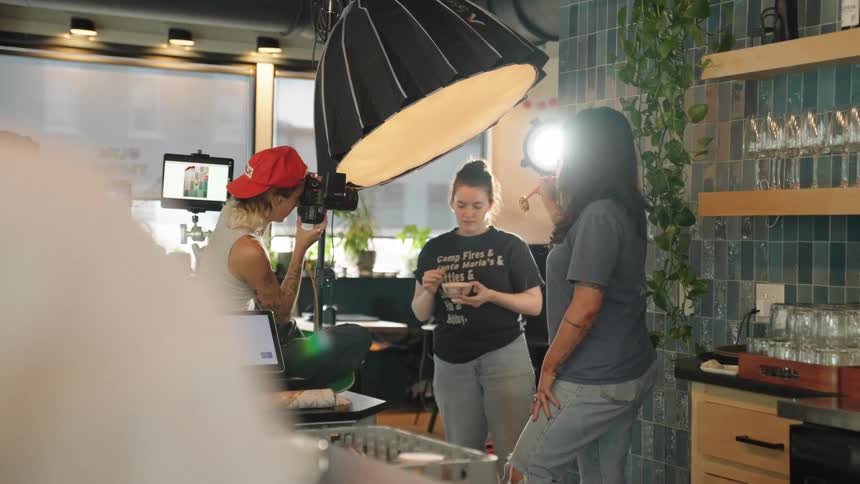 Three women in a photography studio and one of them is taking a picture of an object held by two others