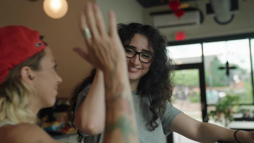 Two women give each other a high five in a restaurant