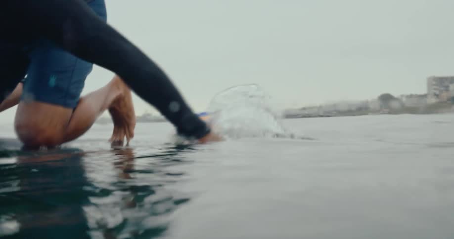 A person surfing on a yellow board crouched low picking up trash from the ocean