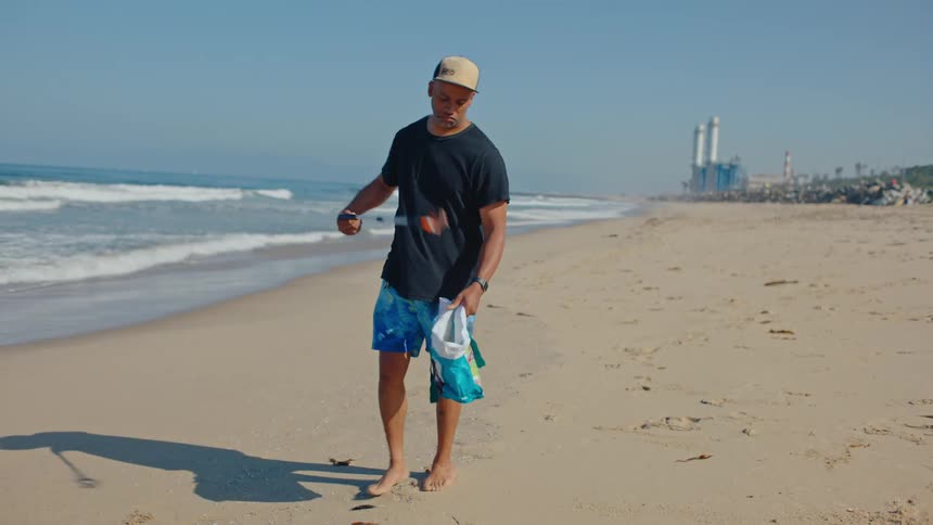 A man collecting garbage from the beach using a clamp near the shoreline