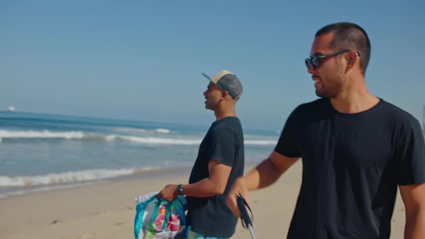 Two people walk on a beach picking up trash