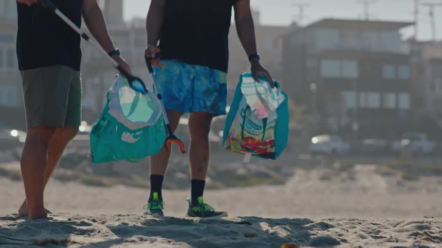 Two men on a beach picking up trash in the sand