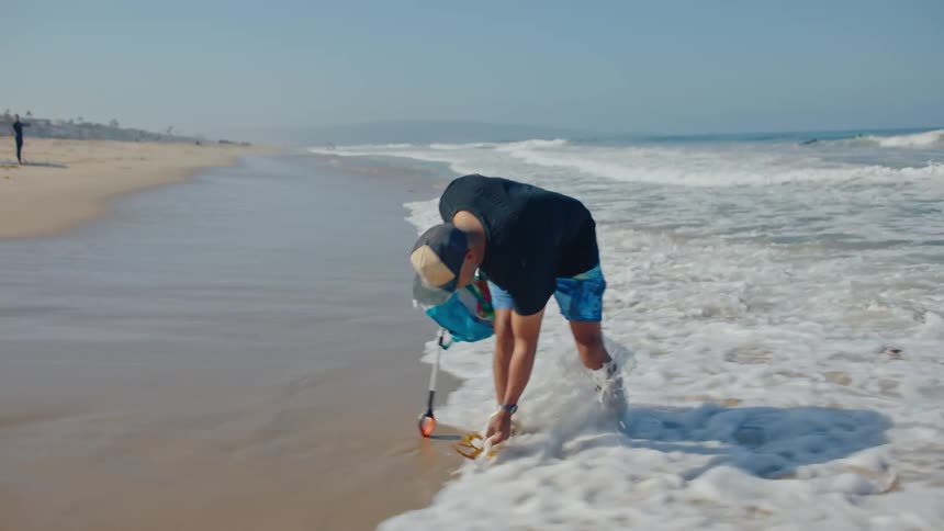 A man is picking up trash on the beach