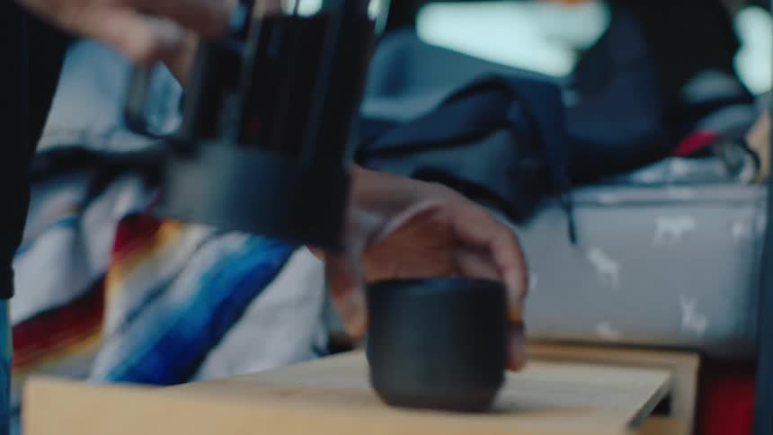 Hand holding a bottle and pouring coffee into a black ceramic cup
