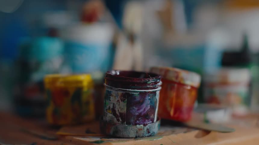 A closeup view of small used paint pots with visible paint stains arranged on a shelf alongside other art supplies
