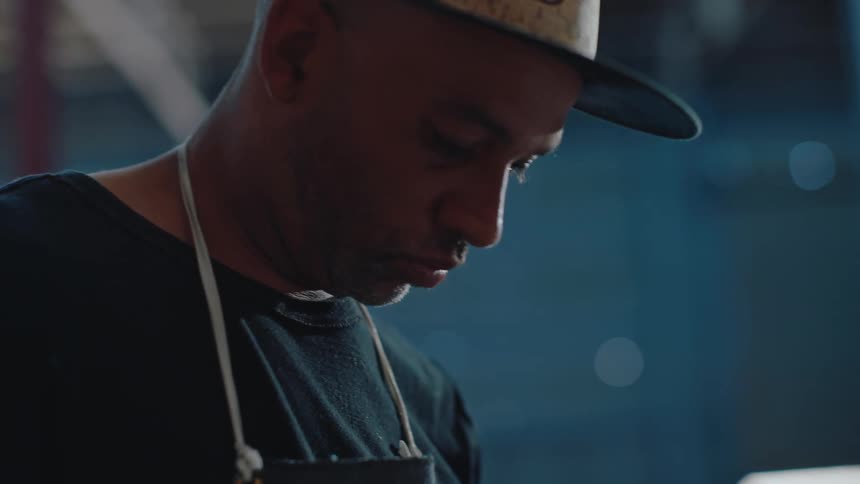 A man in a cap is looking down where he is holding a bucket and is stirring an object inside the bucket