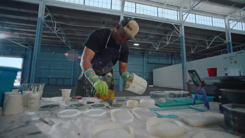 A man wearing an apron pours colored liquid into silicone molds