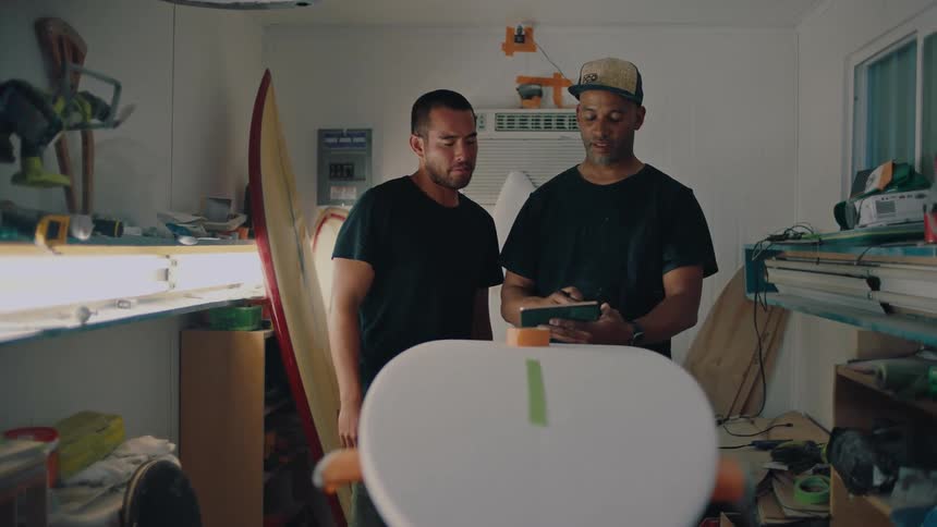 Two men talk while examining a surfboard