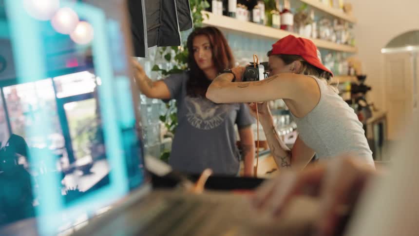 A woman holding a red object and another woman wearing a red cap is taking pictures using a professional camera