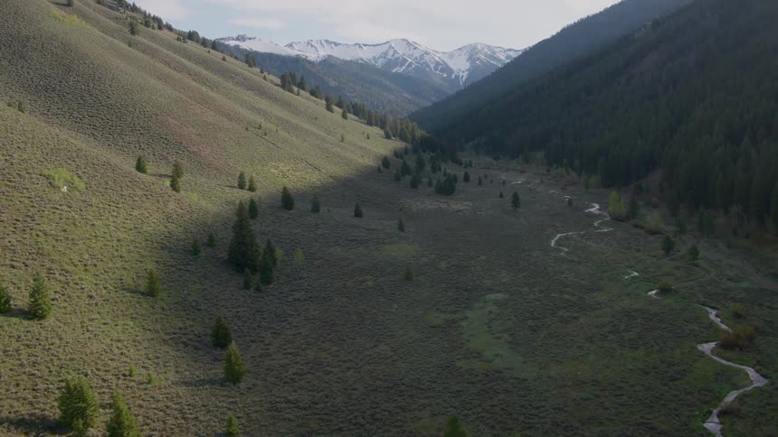 Tilt up reveal of a dramatic mountain valley with a narrow winding river and snow capped peaks in the distance