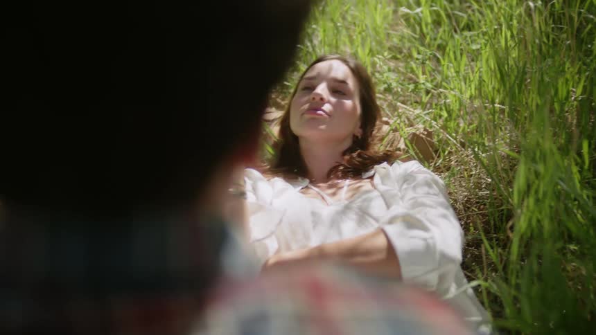 Woman lying in a grassy field holding a yellow flower and in front of her a man sitting