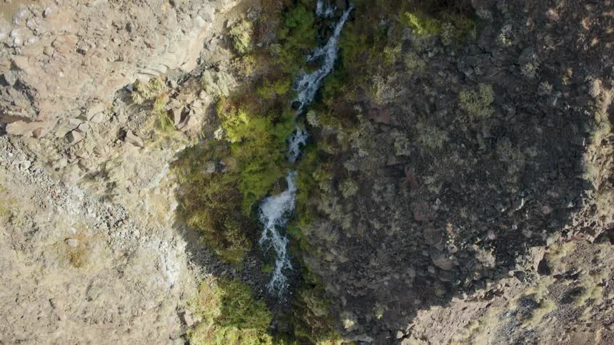 Top down view of a waterfall that cuts through an arid desert cliff side