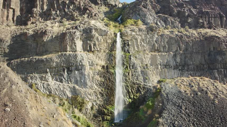 Approach towards a tall waterfall cascading down a rugged desert cliff