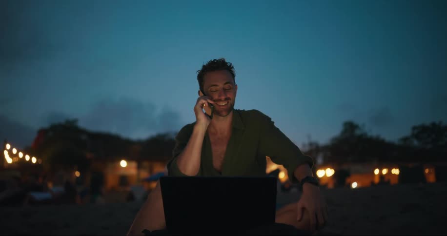 A man is talking on his his cell phone while using a laptop outside