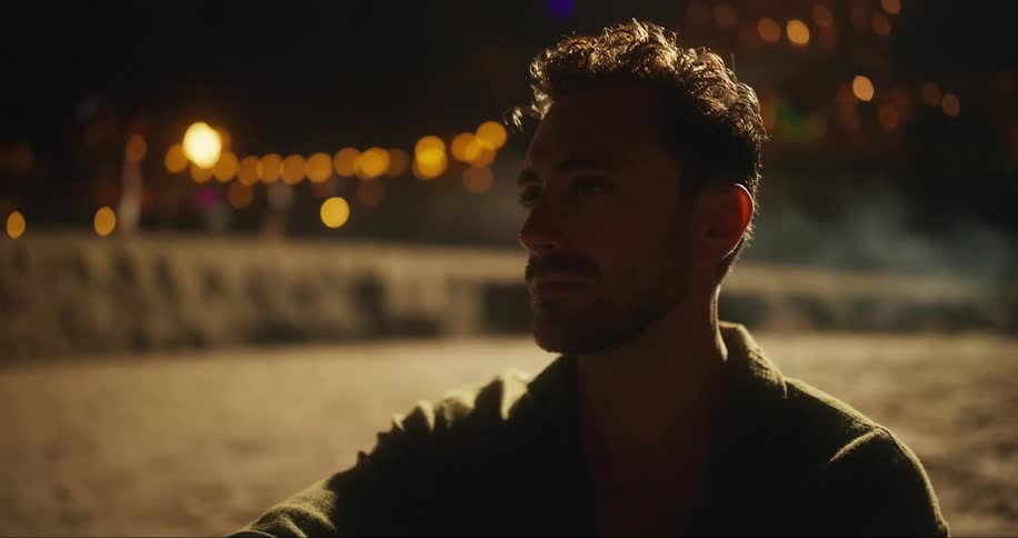 Man on sand watching and blurred lights in the background at night