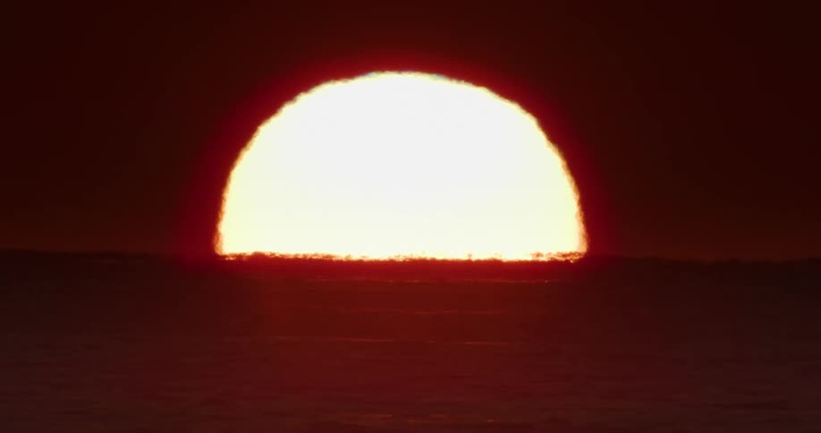Landscape of the sun on the horizon rising above sea level against a dark reddish sky