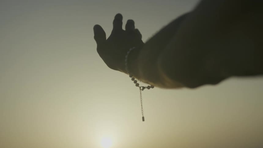 An extended hand with bracelet against a serene sunrise or sunset backdrop
