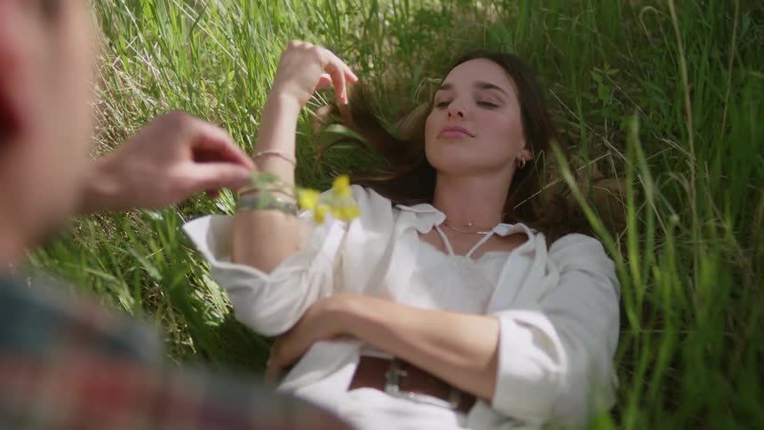 Woman lying in a field with tall grass and a man handing her a yellow flower
