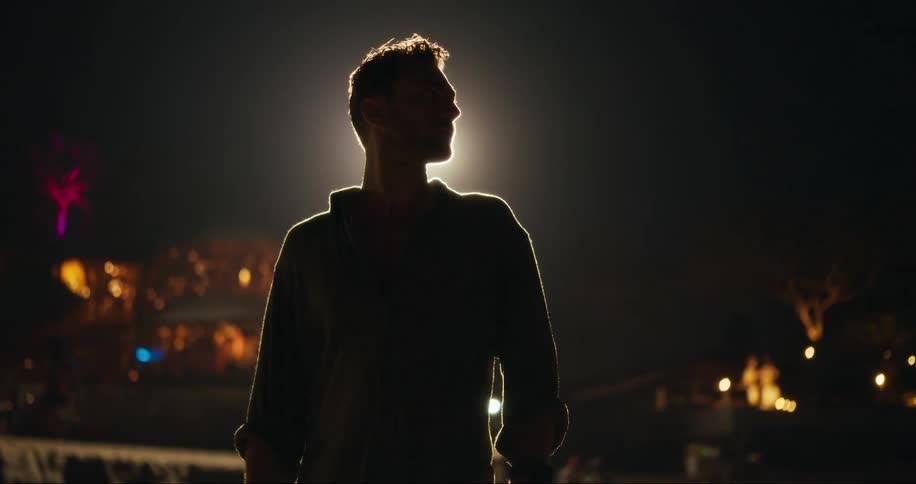 Silhouette of a man outdoors at night and a nightclub in the background