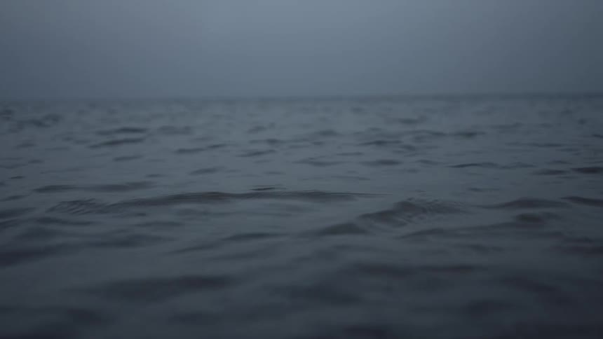 Calm waves in the middle of an ocean beneath a dimly lit sky
