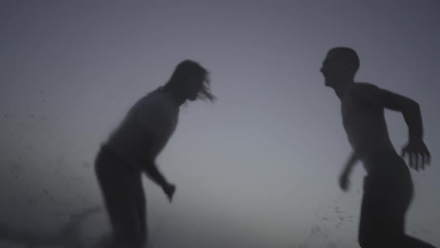 Silhouette of two people running after each other in the sea water