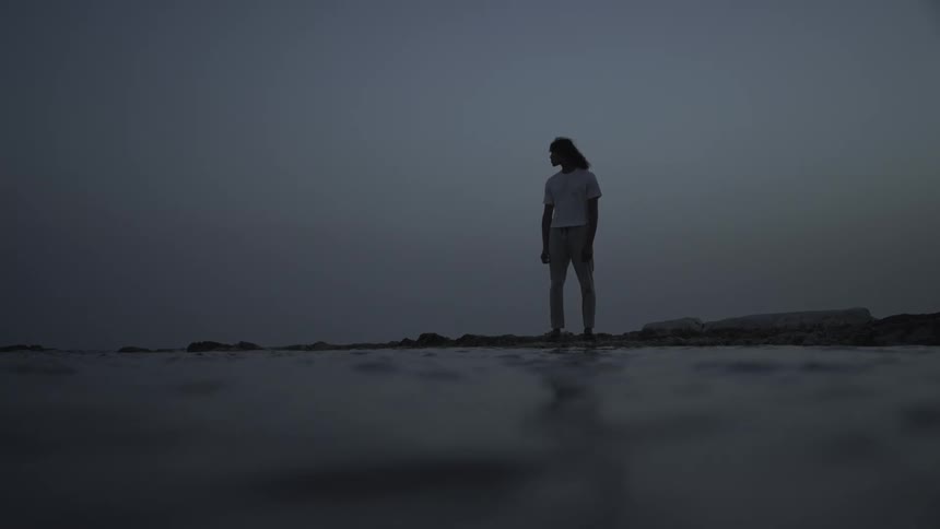 A man is standing on the beach at sunset