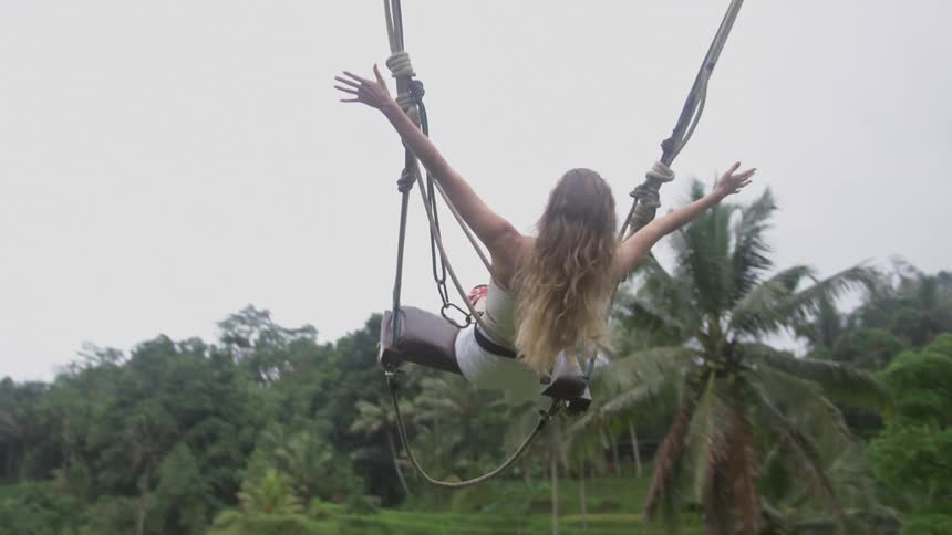 Woman with open arms having fun on a swing surrounded by tropical palm trees