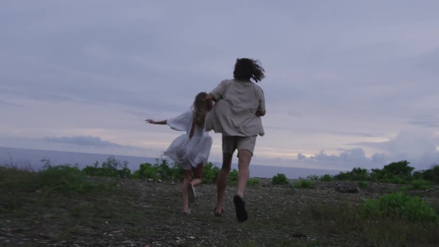 View of a man and a woman running across a field holding hands