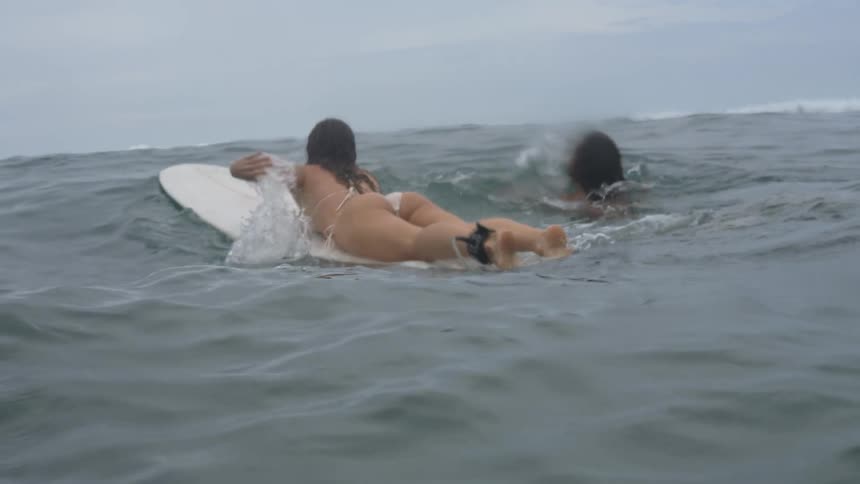 A woman on a surfboard paddles out into the ocean
