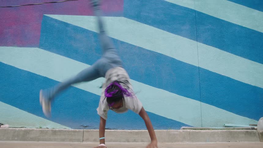 A woman doing a cartwheel against a blue and purple geometrically patterned wall